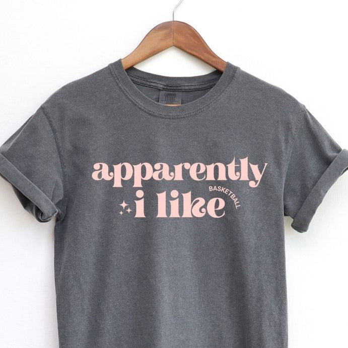Gray t-shirt with 'apparently i like' text on a hanger against a white background